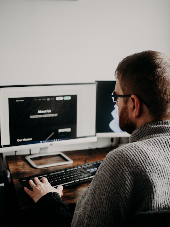 Man working on web design at home office setup with dual monitors.